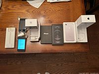 All items laid out: adapter package, two iPhones with cables, five iPhone boxes showing contents