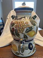 Front view of ceramic sangria jug on bowl stand displaying fruit motif and lid