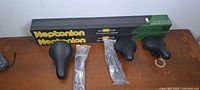 Two boxed Neptonion HO T5 UVB terrarium hoods, three black bicycle seats, two bagged power cords on tabletop
