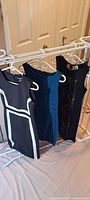 Three dresses on hangers: black with white trim, teal, black with lace panel