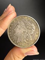 Obverse of 1921 Morgan dollar held between fingers, showing Liberty head, date, motto, and edge detail