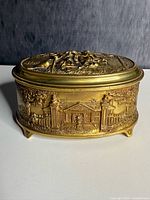Front view of oval gilt bronze jewelry casket showing lid relief and side scenic panels