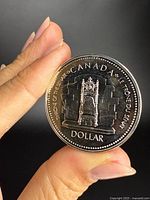 Front view of Canadian silver dollar coin held between fingers showing throne design and inscriptions