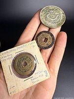 Obverse views of three coins in hand: dragon coin, loose bronze cash coin, Qianlong cash coin in flip