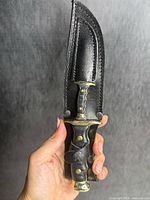 Knife in sheath held upright showing handle, guard, pommel and sheath details