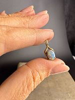 Close-up of vintage 10K yellow gold pendant with oval cabochon opal held between fingers