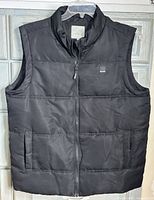 Front view of black Bench puffer vest hung on hanger