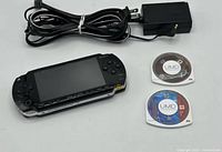 Front view of PSP console, charger, two UMD discs