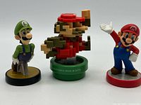 Front view of the three Amiibo figures: Luigi, 8-Bit Mario, Mario