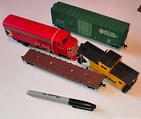 All four HO-scale train cars laid out with pen for scale