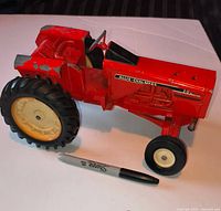 Left side view of red metal Allis-Chalmers 190XT toy tractor beside Sharpie for scale