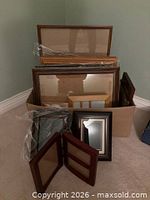 Box containing assorted picture frames of various sizes and finishes, some wrapped in plastic