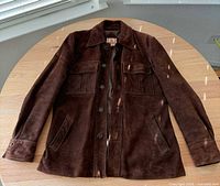 Full front view of brown suede jacket laid flat showing collar, button front, pockets, cuffs