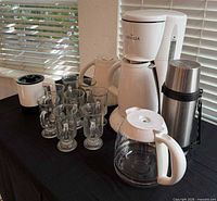 Overview of Gevalia coffee maker, glass pot, insulated and stainless carafes, grinder, and eight pedestal mugs