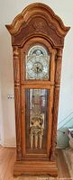 Full frontal view of oak grandfather clock showing pediment, dial, glass door and base