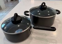 Two black non-stick pots with lids shown on countertop