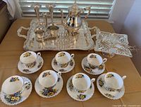 Overview of all items: teacups, saucers, silver tray, coffee pot, pedestal tray, candlesticks, small bowls, pierced tray, serving tools