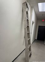 Ladder folded against wall showing full height and weathered wood