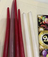 Four red and two white taper candles beside sparklers package