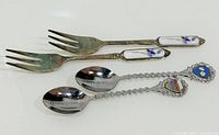 Two metal spoons and two porcelain-handled forks laid out on white surface