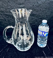 Full view of clear glass pitcher beside water bottle for scale