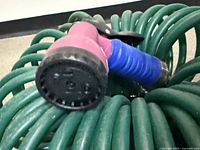 Coiled green hose with attached pink and blue spray nozzle