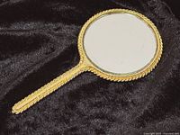 Front view of gold-tone handheld mirror showing mirror surface and decorative handle