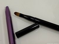 Close-up of purple and black brushes, one brush cap removed to show bristles