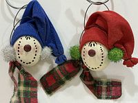 Both snowman head ornaments side by side showing hats, faces, scarves and hanging loops