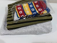 Stacked view of folded cardigan, folded sweatshirt and sealed socks