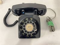 Front view of black rotary desk telephone with handset resting on cradle, rotary dial visible