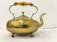 Right profile of brass teapot showing spout, feet and handle