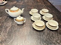 Top-down view of entire tea set on dark surface showing teapot, sugar bowl, six cups and saucers