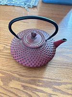 Full view of red cast iron teapot with black handle and lid