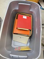 Plastic storage tote containing cardboard box of binders and papers