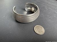 Wide sterling silver cuff bracelet beside quarter for scale