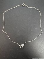 Full view of sterling silver necklace laid flat showing chain and bow pendant