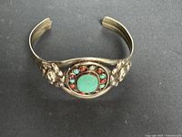 Top view of brass-tone cuff showing central green stone and surrounding cabochons