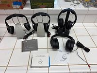 Three Sennheiser wireless headphone sets, one black wireless headphone on stand, one wired headphone with cable, manuals