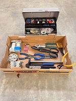 Overall view of cardboard box containing hand tools, metal parts and packaged fittings, plus closed plastic toolbox