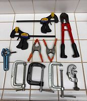 Top overview of all clamps, bolt cutter and pipe cutter laid on tiled surface