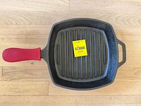 Top view of Lodge square cast iron grill pan with red silicone grip and product tag