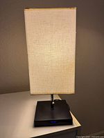 Table lamp showing black square base, linen rectangular shade, USB ports