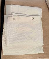 Folded white textured shower curtain showing silver grommets