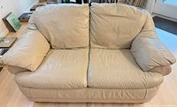 Front view of tan leather loveseat showing attached cushions and pillow arms