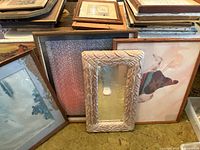 Stacked framed art and mirrors showing variety of frames, leaf-pattern mirror centered