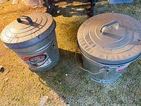 Two galvanized trash cans with lids, left can shows Behrens label