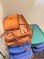 Cardboard trays showing tan leather straps, small unfinished purse on top of plastic totes
