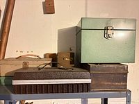 Shelf with beige toolbox, brown ridged case, speckled green cube box and rusted box