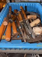 Top view of blue bin containing assorted chisels, gouges, mallets, rasps, small saw blade